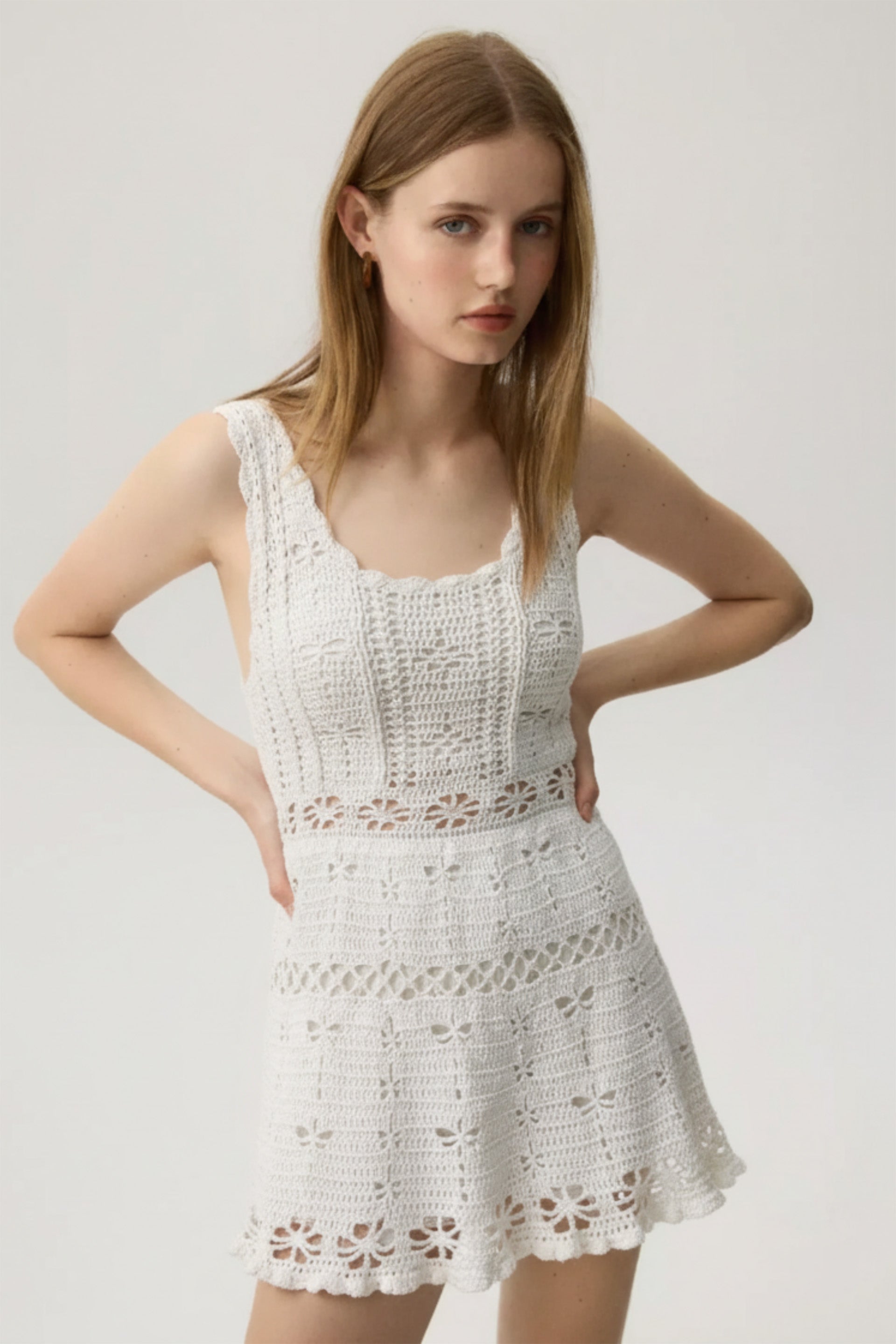 Woman wearing a white crochet dress against a plain background
