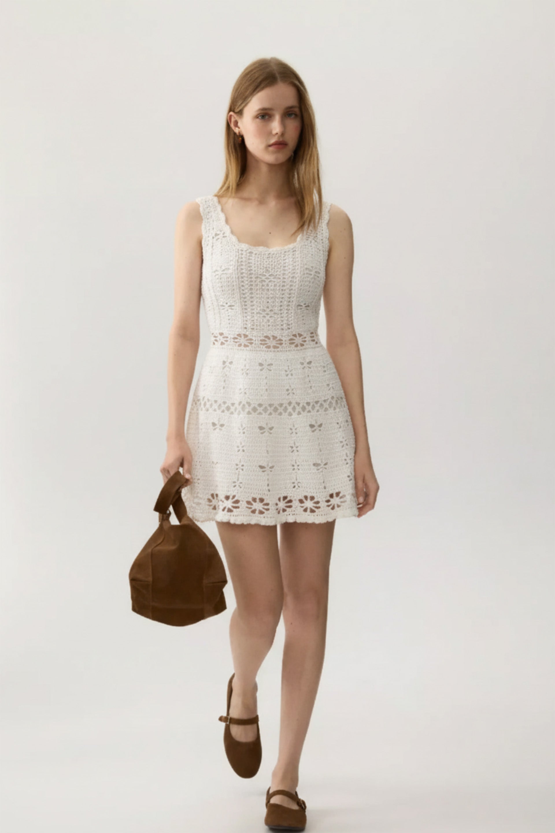 Woman wearing a white lace dress holding a brown bag on a white background