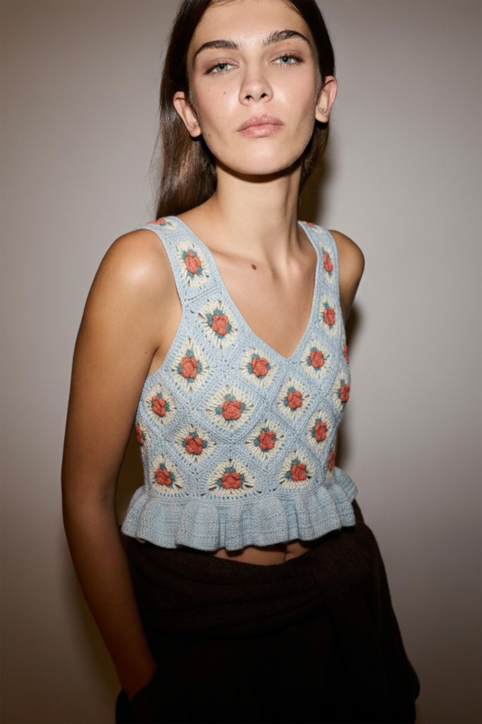 Woman wearing a light blue floral crochet top against a neutral background