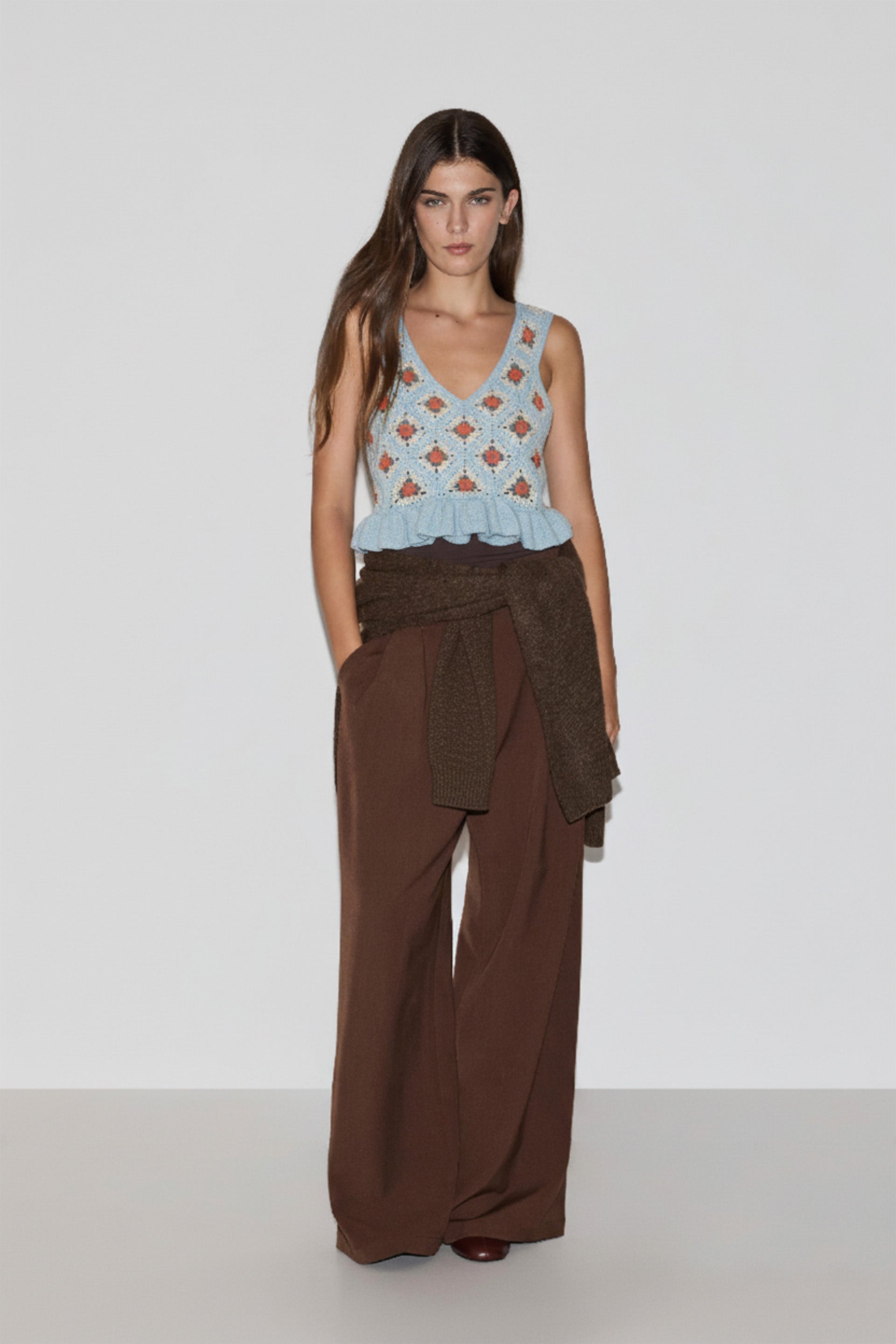 Woman wearing a light blue patterned top and brown wide-leg pants on a white background