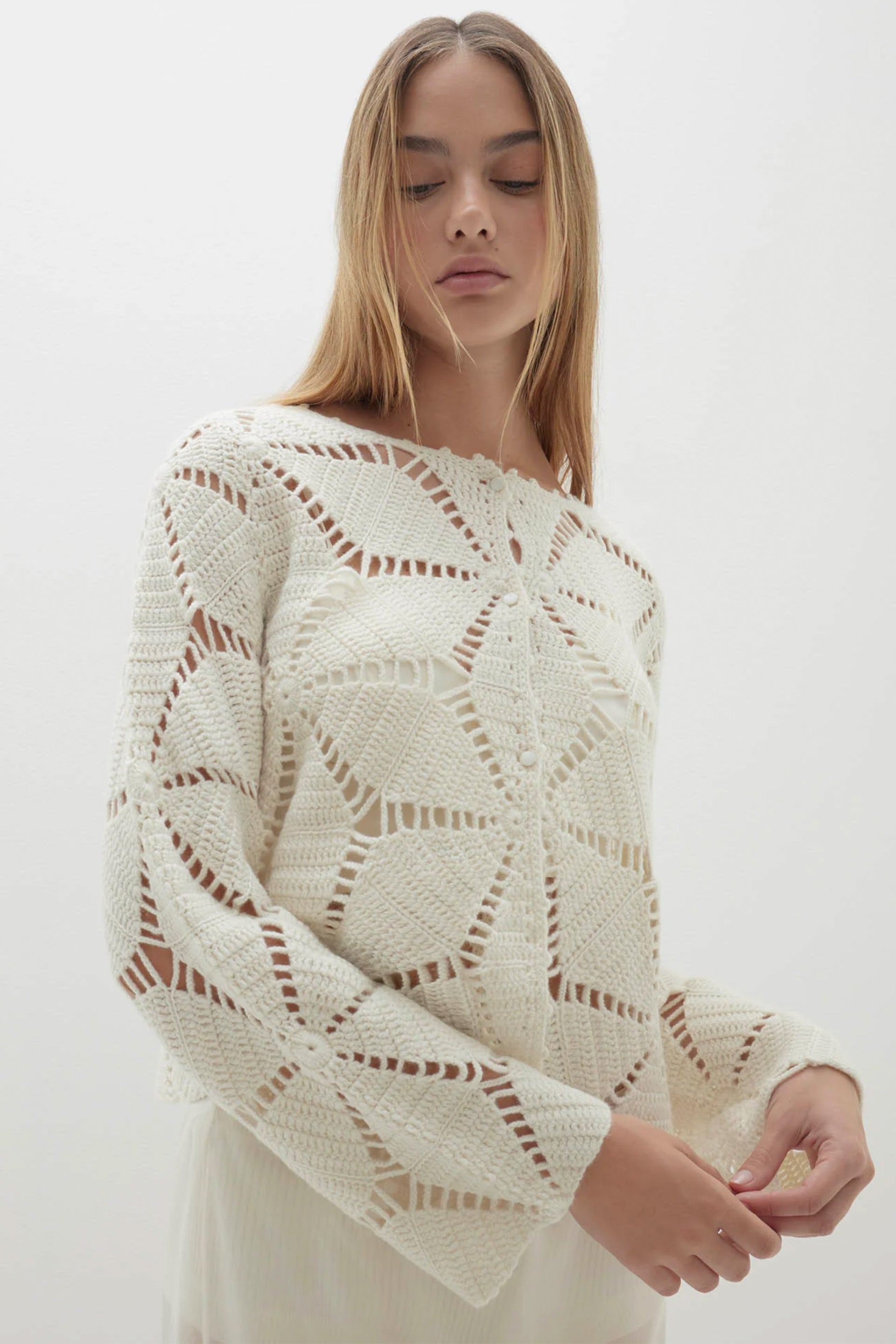 Woman wearing a cream-colored knit sweater with a geometric pattern on a white background